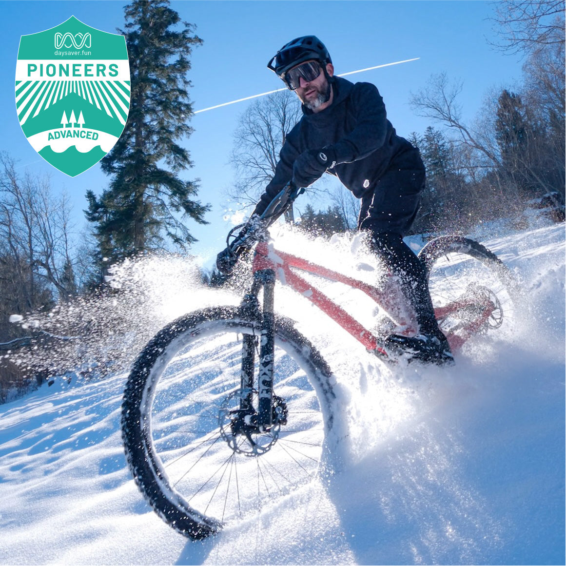 Person riding a bike through deep snow with trees and clear blue sky in the background